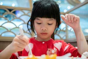 schattig weinig Aziatisch kind meisje aan het eten voedsel foto