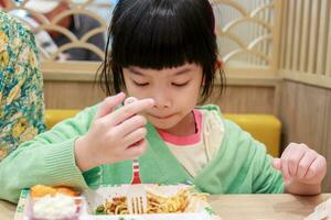 schattig weinig Aziatisch kind meisje aan het eten voedsel foto