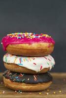 lief zoet voedsel. stack van geglazuurd kleurrijk geassorteerd donuts met spatten Aan een grijs achtergrond. foto