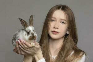 gelukkig jong meisje Holding een wit konijn Aan een grijs achtergrond foto