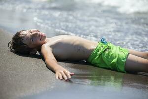 gelukkig jongen is resting door de zee, genieten van de golven en zomer vakantie. kind Aan vakantie Bij de kust. foto