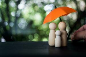 familie van houten poppen zijn schuilplaats onder een oranje paraplu, beschermen houten pin poppen met kopiëren ruimte foto