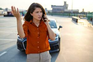 nerveus jong vrouw staand door Open auto kap en roeping naar auto onderhoud, kreeg gebroken Bij snelweg Aan een manier naar platteland. vrouw rit hebben telefoon gesprek met vrienden, vragen voor helpen met auto foto