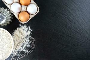 bakken ingrediënten meel, eieren, melk, bakvormen Aan zwart leisteen achtergrond met kopiëren ruimte foto