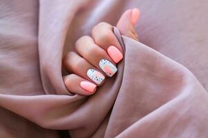 Dames - een hand- met een mooi manicure houdt een zijde kleding stof. voorjaar tendens, roze nagels, tekening Aan nagels met gel Pools, schellak. kopiëren ruimte. foto