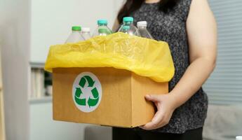 huis recycle eco groen nul concept vrouw het werpen leeg plastic fles in recycling bak met geel vuilnis Tassen Bij huis. foto