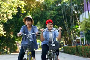 twee Aziatisch jongens wie zijn vrienden rijden fietsen in de lokaal park Aan vakantie. ze zijn beide gelukkig en hebben plezier. vakantie werkzaamheid concept. zacht en selectief focus. foto