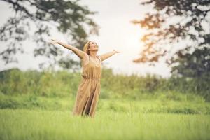 jonge vrouw die in grasveld staat en handen in de lucht steekt. foto