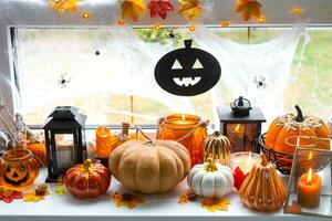 feestelijk decor van de huis Aan de vensterbank voor halloween - pompoenen, jack O lantaarns, schedels, spinnenwebben, spinnen, skeletten, kaarsen en een slinger - een knus en vreselijk humeur foto