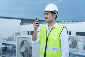 Aziatisch onderhoud ingenieur werk Aan de dak van fabriek. aannemer inspecteren compressor systeem en plannen installatie van lucht staat systemen in bouw. technologie, walky spraakzaam, onderhoud foto