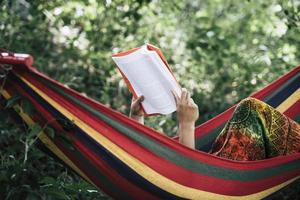 jonge vrouw die een boek leest dat in een hangmat ligt