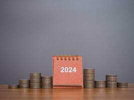 2024 bureau kalender met stack van munten. de concept van besparing geld, financieel, investering en bedrijf groeit in nieuw jaar 2024. foto