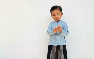 een schattig weinig jongen met blauw overhemd en sarong bidden foto
