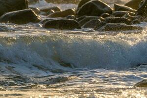 golven breken Aan strand gedurende zonsondergang foto