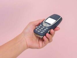 dichtbij omhoog hand- Holding mobiel telefoon nokia 3310 geïsoleerd Aan roze achtergrond. vrouw hand- Holding oud gebruikt telefoon nokia 3310. foto
