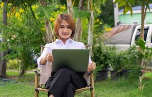 zakenvrouw zittend Aan stoel Bij de tuin en gebruik makend van apparaat laptop verzonden e-mail en kijk maar online sociaal media. foto