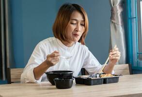 vrouw zittend Bij stoel genieten aan het eten heerlijk reeks doos voedsel hebben meenemen Bij huis ontspannende resting en gelukkig levensstijl concepten foto