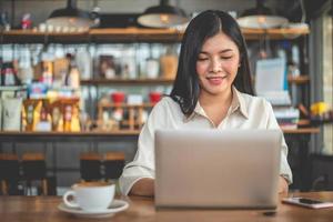 Aziatische vrouwelijke freelancer lacht bij het gebruik van laptop in café foto