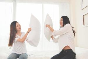 twee Aziatische meisjes doen kussengevecht in de slaapkamer als kindertijd foto