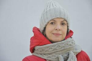 een jong vrouw in een rood jasje en een gebreid beige hoed, sjaal en wanten. vrouwen winter hoeden en accessoires. foto