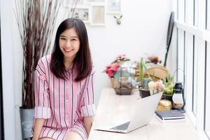 jonge aziatische vrouw die aan laptop werkt die bij koffiewinkel zit. foto