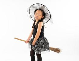portret Aziatisch meisje gekleed in schattige heks die op de bezem rijdt foto