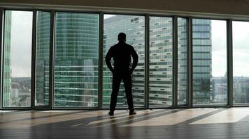 een zelfverzekerd Mens benaderingen de venster tegen de backdrop van wolkenkrabbers. een Mens in een pak in de kantoor tegenover een panoramisch venster. foto