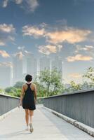 vrouw oefening wandelen in stad park Aan de brug met fles water in haar hand. foto