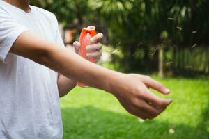 jong jongen sproeien insect insectenwerende middelen Aan huid in de tuin met mug vliegen. foto