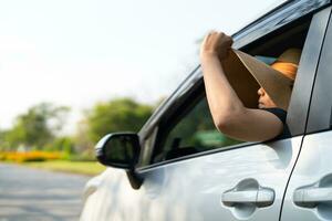 gelukkig genieten en vrijheid in op reis reis met verheven hand- en Holding hoed buiten van venster auto in zomer vakantie vakantie. foto