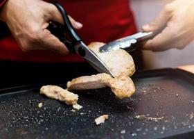 Handgreepschaar die gegrilde varkenssteak snijdt foto