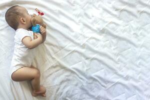 6-8 maanden oud baby jongen aan het liegen speels in bed. charmant 6-7 maand weinig baby in wit bodysuit. baby jongen in wit beddengoed. kopiëren ruimte foto