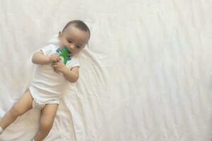 6-8 maanden oud baby jongen aan het liegen speels in bed. charmant 6-7 maand weinig baby in wit bodysuit. baby jongen in wit beddengoed. kopiëren ruimte foto