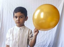 portret van 5-6 jaren oud jongen met ballon. aanbiddelijk midden- oostelijk kind Holding een gouden ballon. vieren, vakantie concept. foto