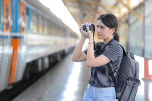 terwijl ze op een trein wacht, draagt een jonge buitenlandse vrouwelijke bezoeker een camera om foto's te maken. foto