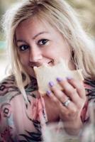 blonde vrouw die een broodje vasthoudt en eet, naar de camera kijkt. close-up portretshoot. foto