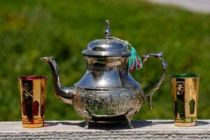 een zilver thee pot en twee kleurrijk cups Aan een tafel foto