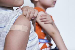 twee jongens tonen hun arm met Zelfklevend verband gips na vaccinatie. injectie covid vaccin, immunisatie voor familie foto