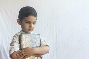 een jong midden- oostelijk jongen met de heilig koran. portret van 5 jaren oud moslim kind Holding een heilig koran met wit achtergrond. vrij ruimte foto