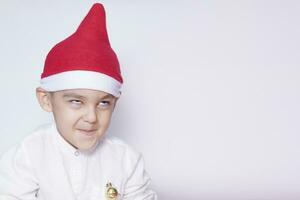 portret van een zes jaar oud jongen tegen de wit achtergrond. vieren kerstmis. 6-7 jaar oud kind met de kerstman hoed. foto