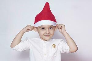 portret van een zes jaar oud jongen tegen de wit achtergrond. vieren kerstmis. 6-7 jaar oud kind met de kerstman hoed. foto