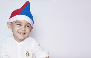 portret van een zes jaar oud jongen tegen de wit achtergrond. vieren kerstmis. 6-7 jaar oud kind met de kerstman hoed. foto