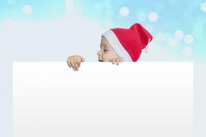 een weinig jongen met de kerstman pet Holding de blanco papier. de kerstman baby jongen met een leeg wit kaart. kopiëren ruimte voor uw reclame en tekst foto