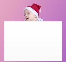 een weinig jongen met de kerstman pet Holding de blanco papier. de kerstman baby jongen met een leeg wit kaart. kopiëren ruimte voor uw reclame en tekst foto