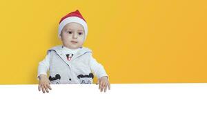 een weinig jongen met de kerstman pet Holding de blanco papier. de kerstman baby jongen met een leeg wit kaart. kopiëren ruimte voor uw reclame en tekst foto