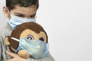 weinig peuter- kind spelen met zijn speelgoed- aap in medisch gezicht masker foto