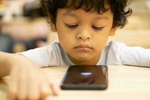 schattig Aziatisch weinig jongen is spelen een spel Aan smartphone foto