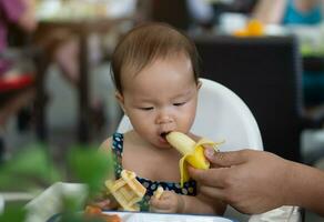 schattig Aziatisch kleuter baby meisje aan het eten banaan foto