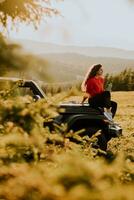 jonge vrouw ontspannen op de motorkap van een terreinvoertuig op het platteland foto