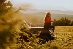 jonge vrouw ontspannen op de motorkap van een terreinvoertuig op het platteland foto